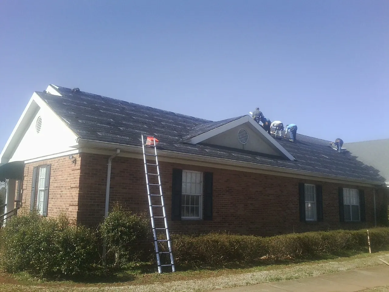 Crew tearing shingles off a brick ranch roof with a ladder set — Metal Roof Repair work by our crew in Belchertown