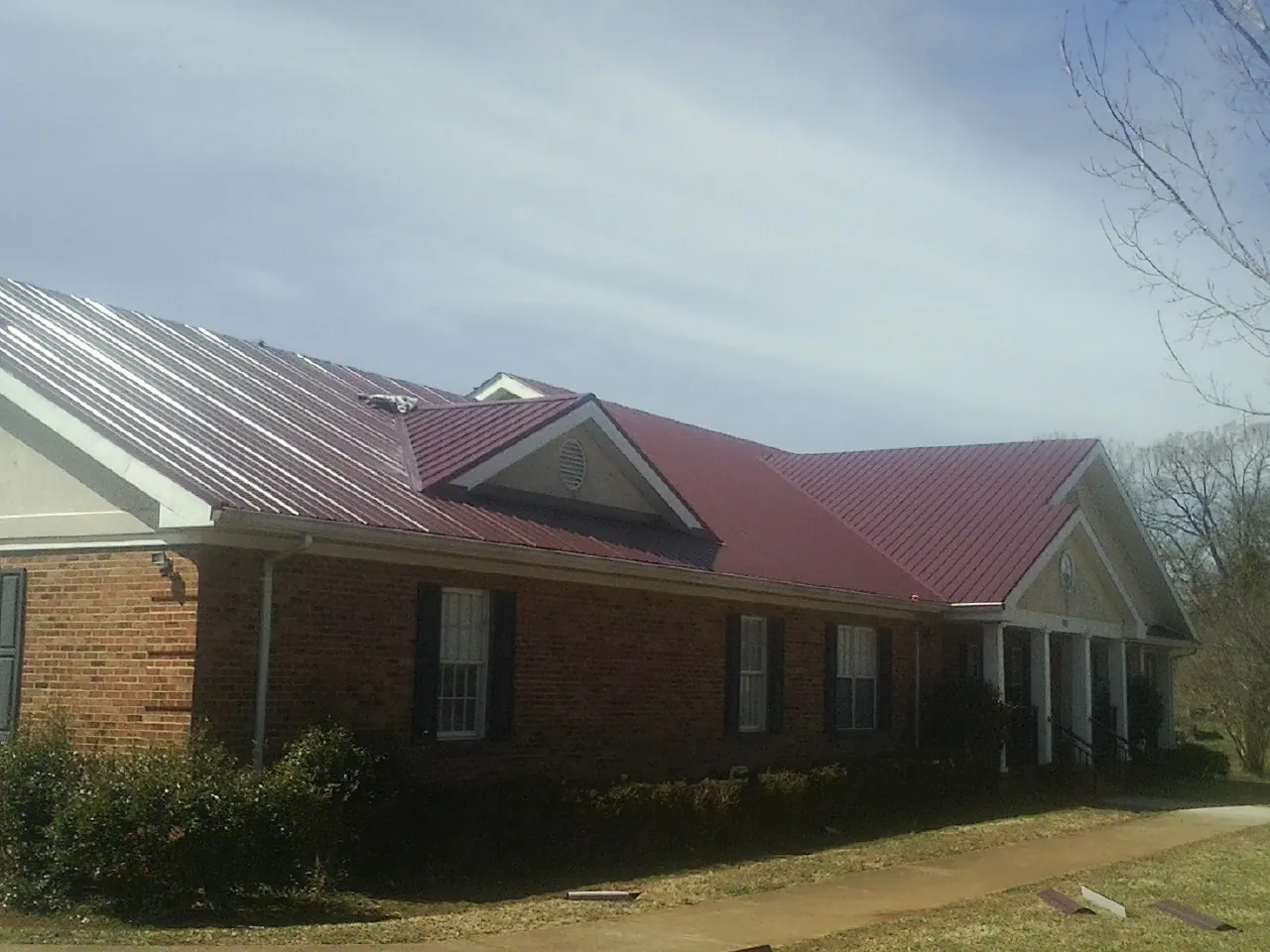 Red metal roof with gabled entries on a long brick building, from a Hail Damage Roof Repair job in Belchertown