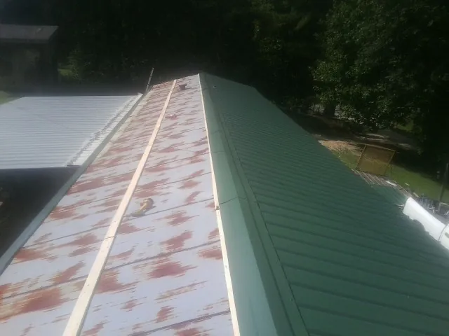 Old rusted panels beside newly installed green metal roofing — Wind Damage Roof Repair by Roofing Brothers in Belchertown