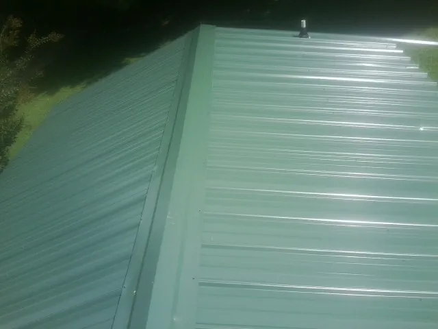 New green metal panels meeting at the ridge of a roof — Flat Roof Repair work by our crew in Belchertown