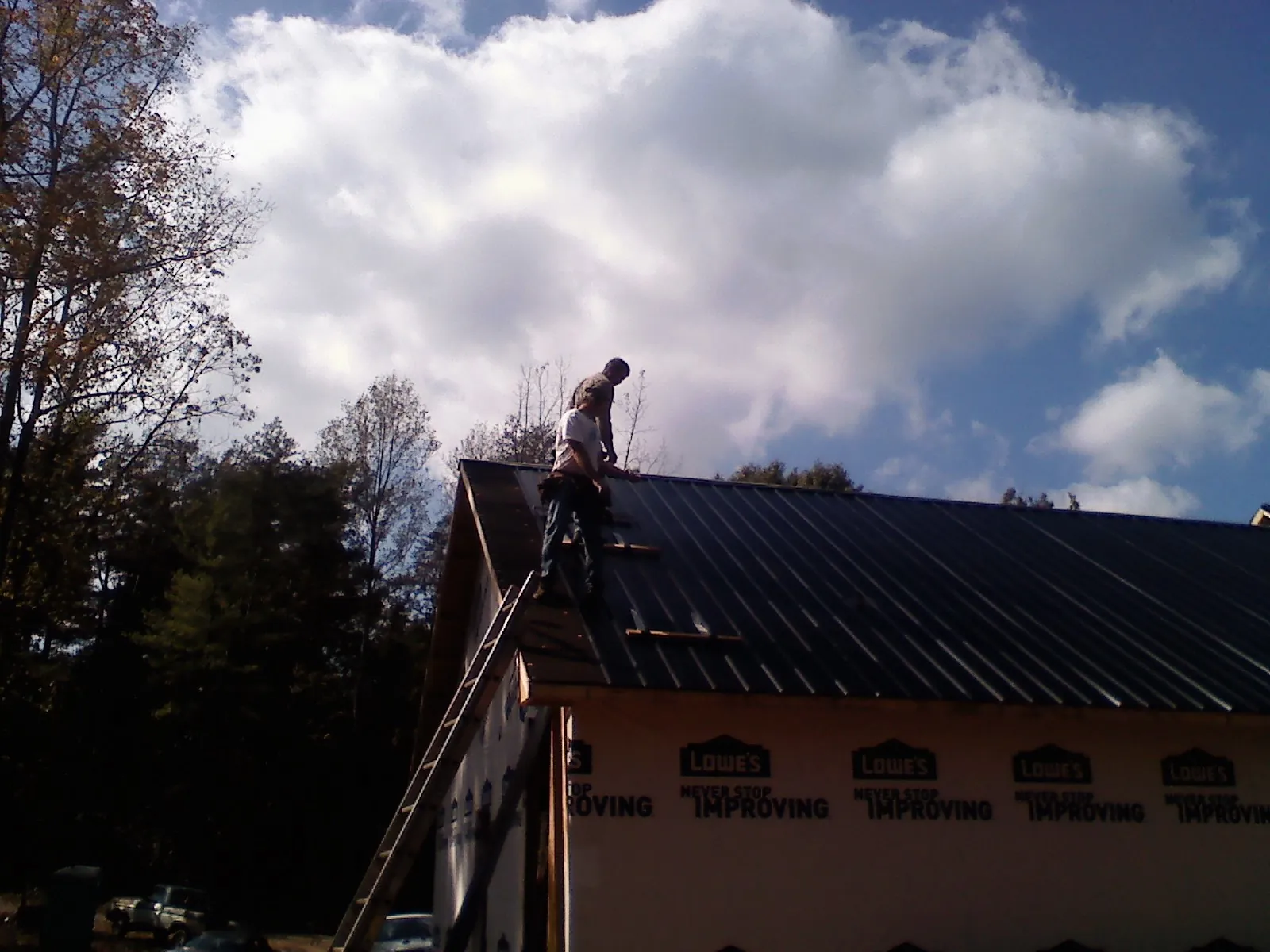 Roofer fastening dark metal panels high against a cloudy sky, from a Roof Inspection job in Belchertown