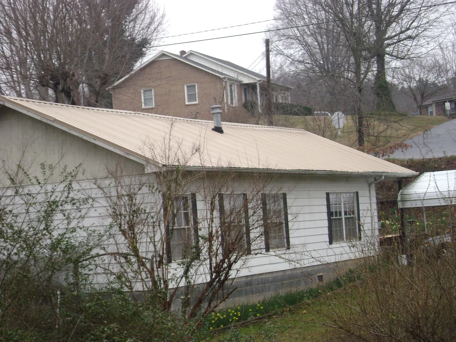 Tan metal roof on a white sided house set into a hillside — Commercial Roofing by Roofing Brothers in Belchertown