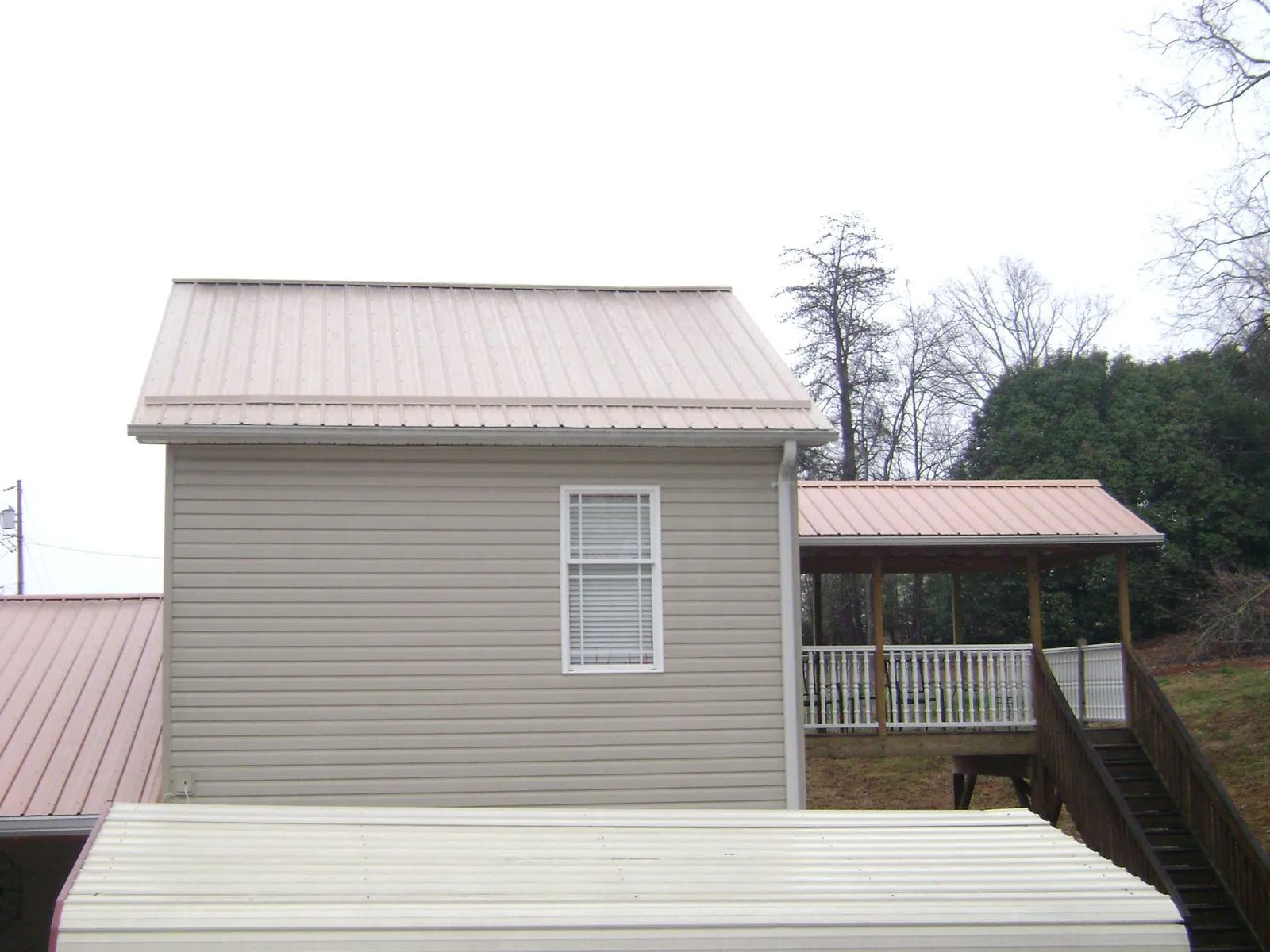 Tan metal roofs on a two story addition and attached porch, from a Roof Replacement job in Belchertown